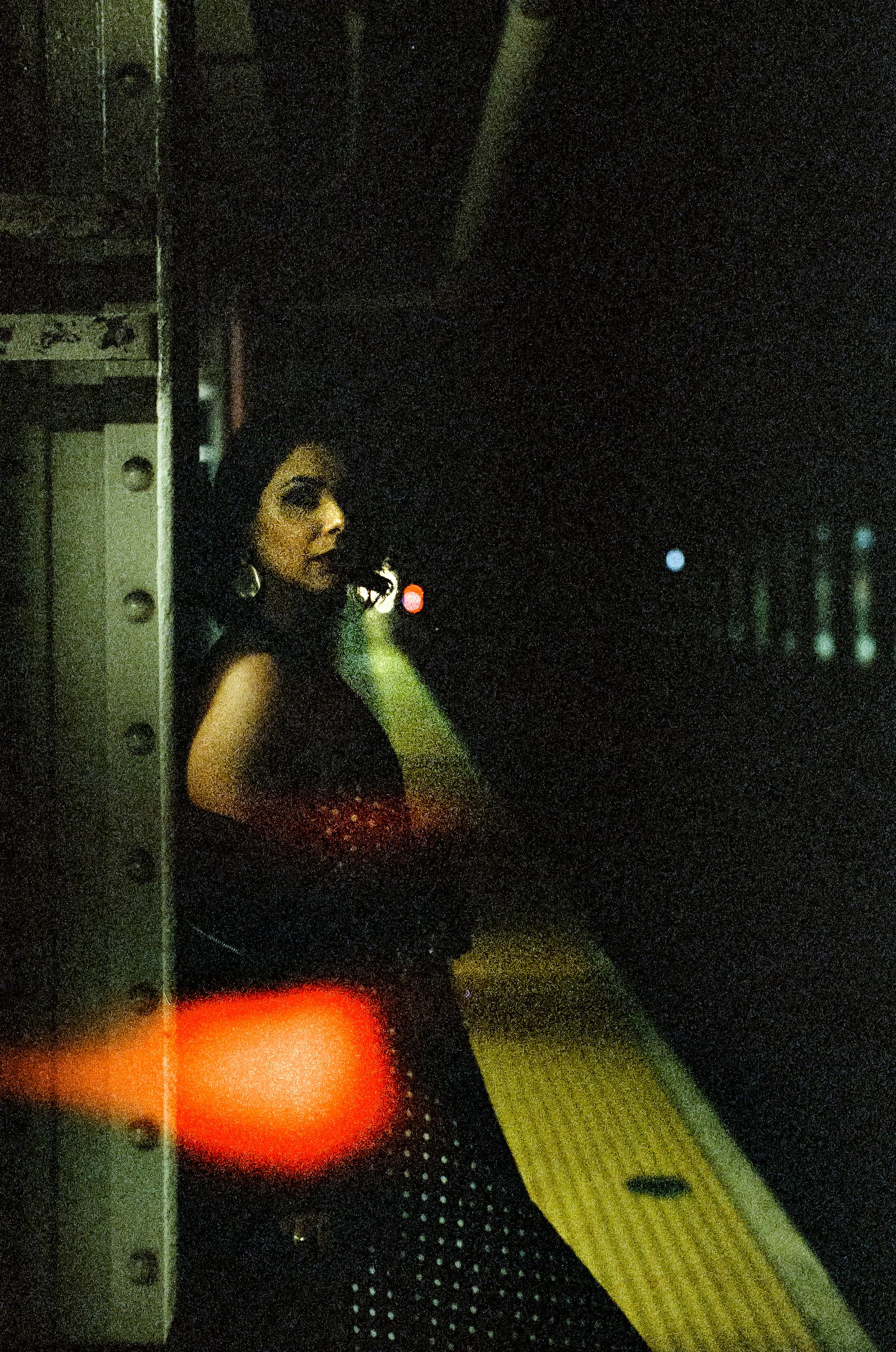 Dark moody photograph of someone on a phone in a subway station with red lighting.