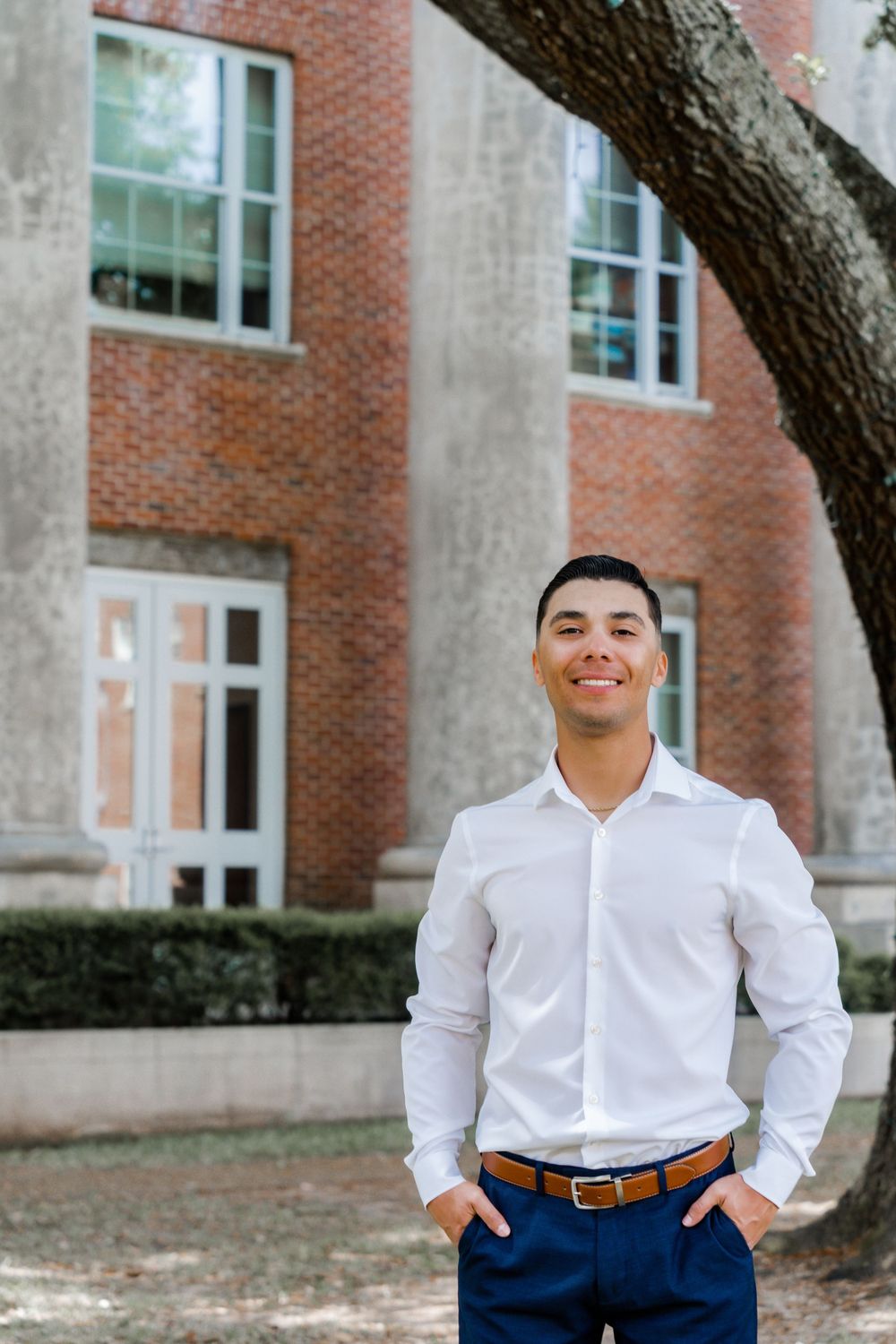Graduate poses in business attire in front of brick university building.