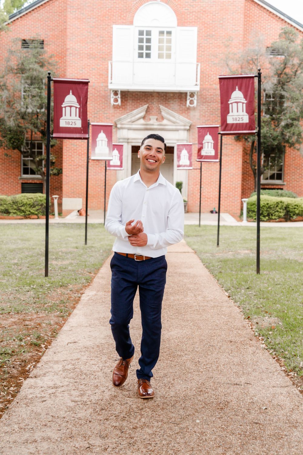 Graduate walks along pathway with university banners and brick building in background.