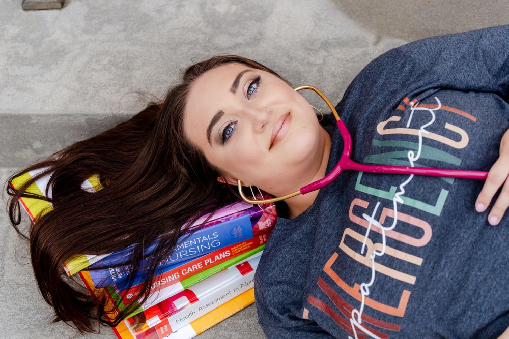 Student lying down with textbooks wearing navy collegiate sweatshirt.