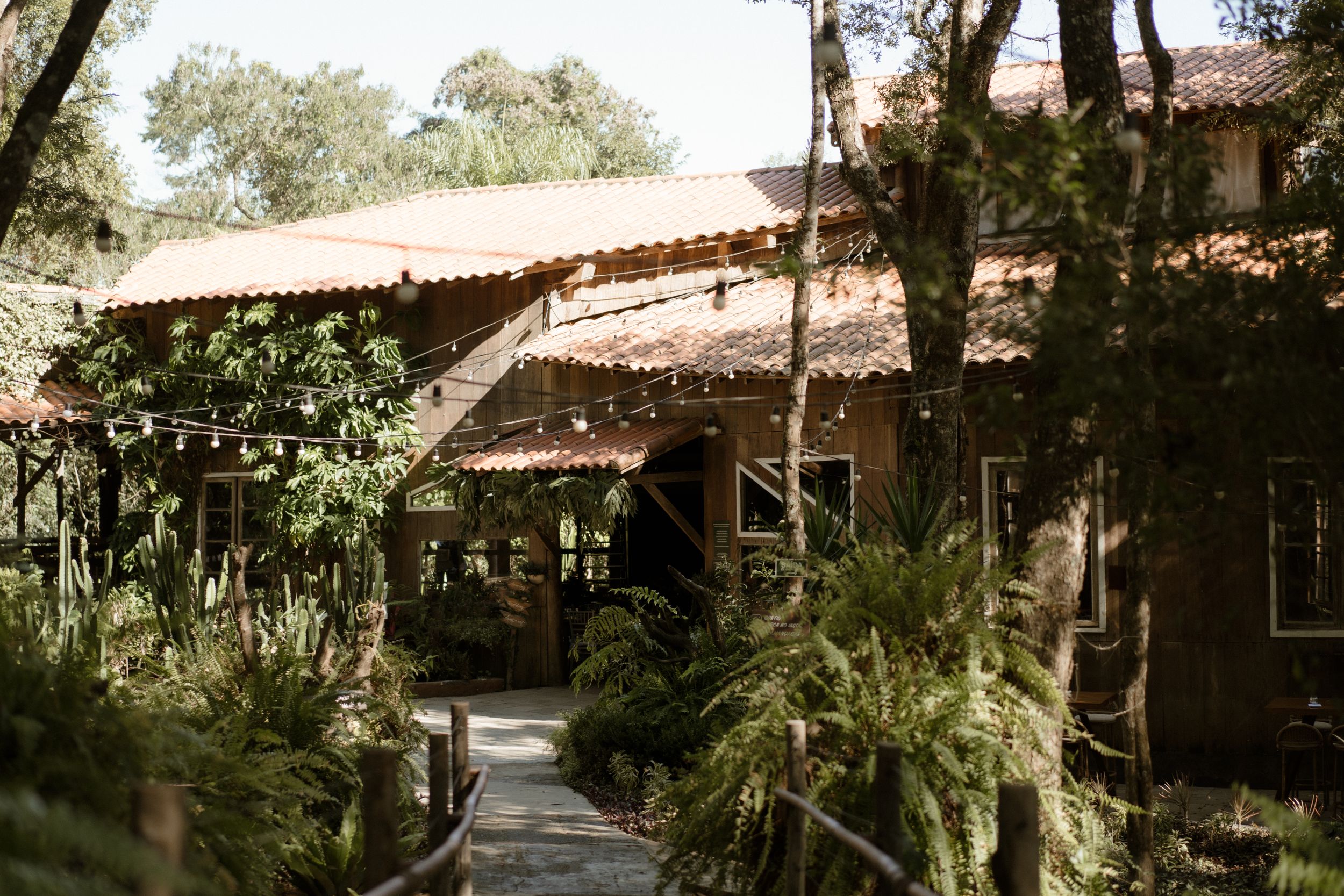Rustic wedding venue with string lights and lush greenery around a covered walkway.