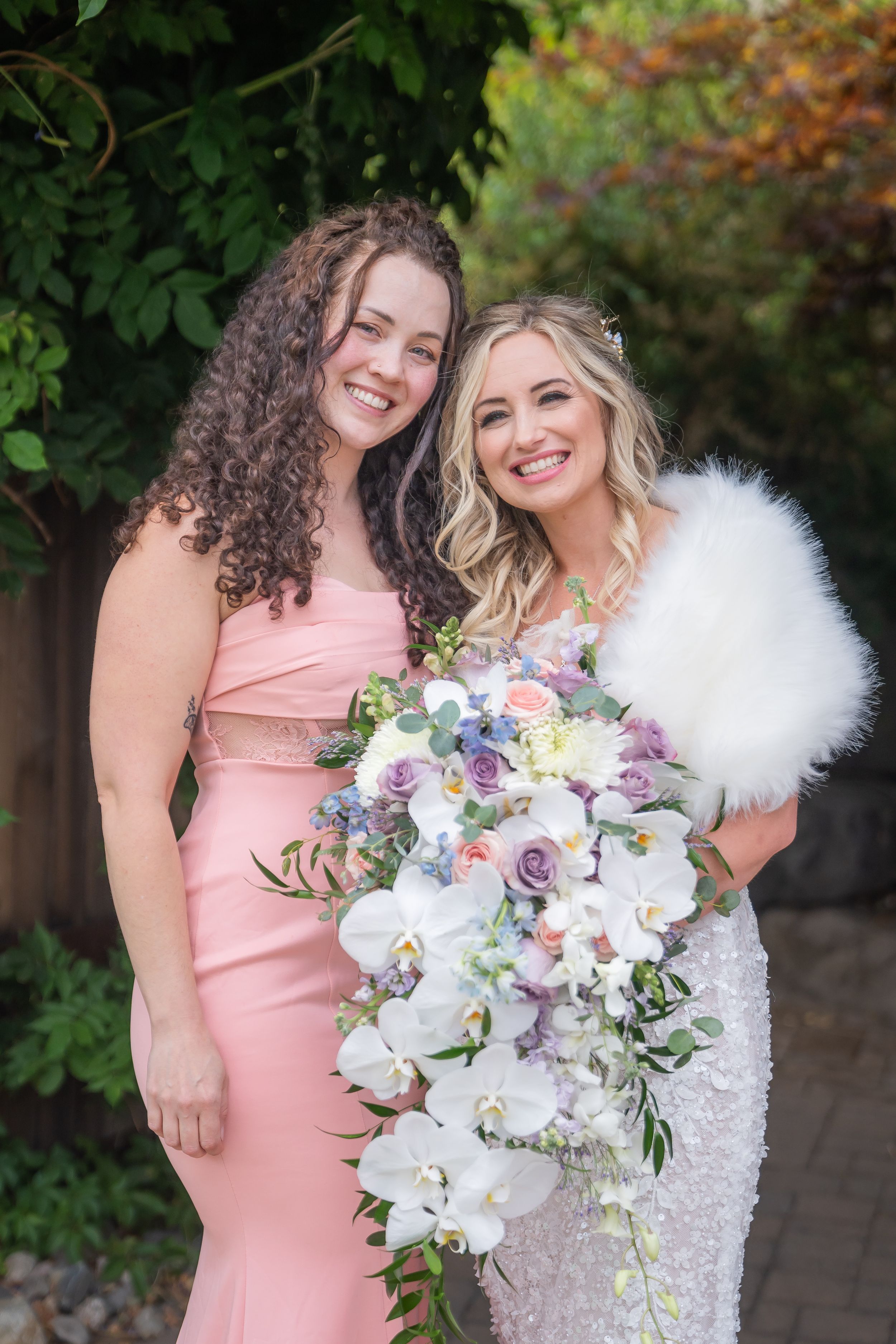 Wedding photo outdoors featuring a pink bridesmaid dress and stunning white orchid and lavender rose bridal bouquet.