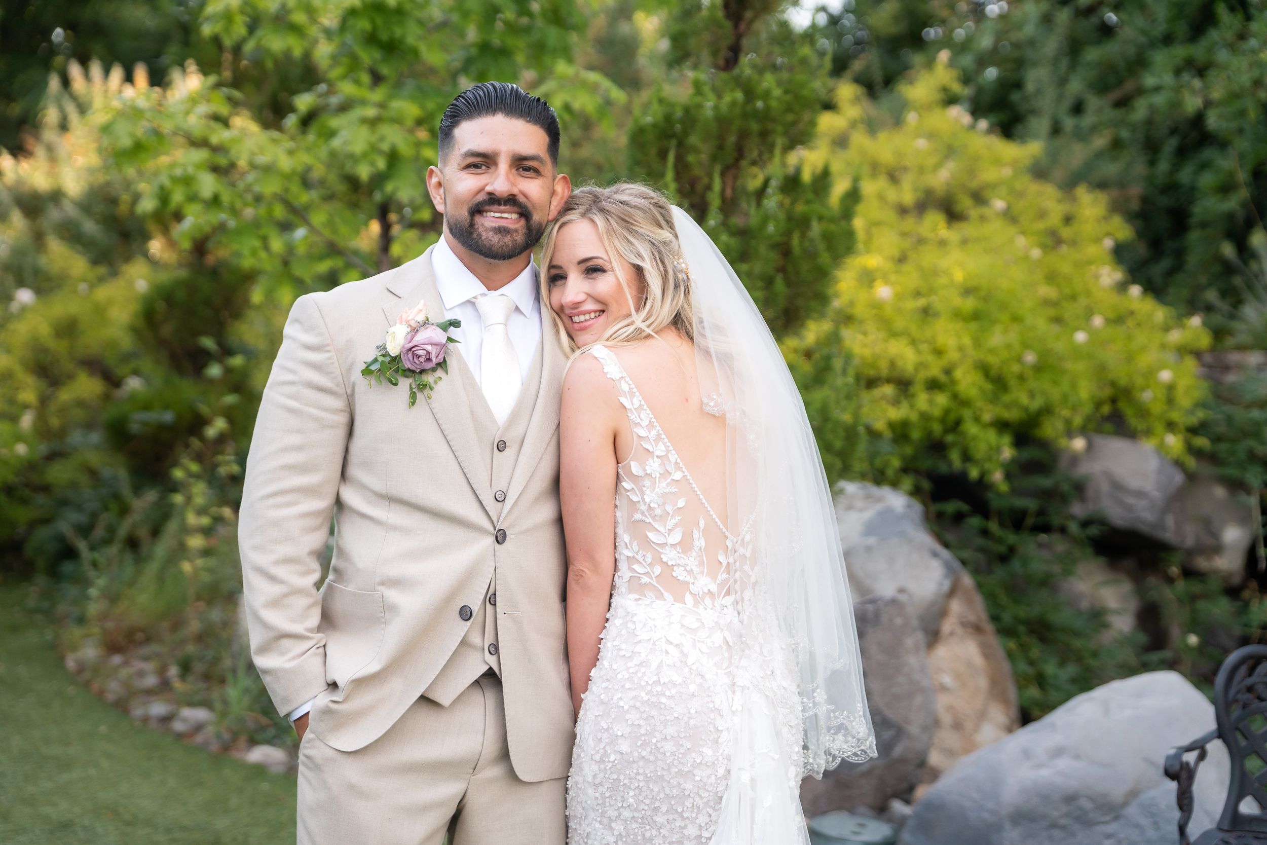 A newlywed couple poses together outdoors in a garden setting with lush greenery in the background.