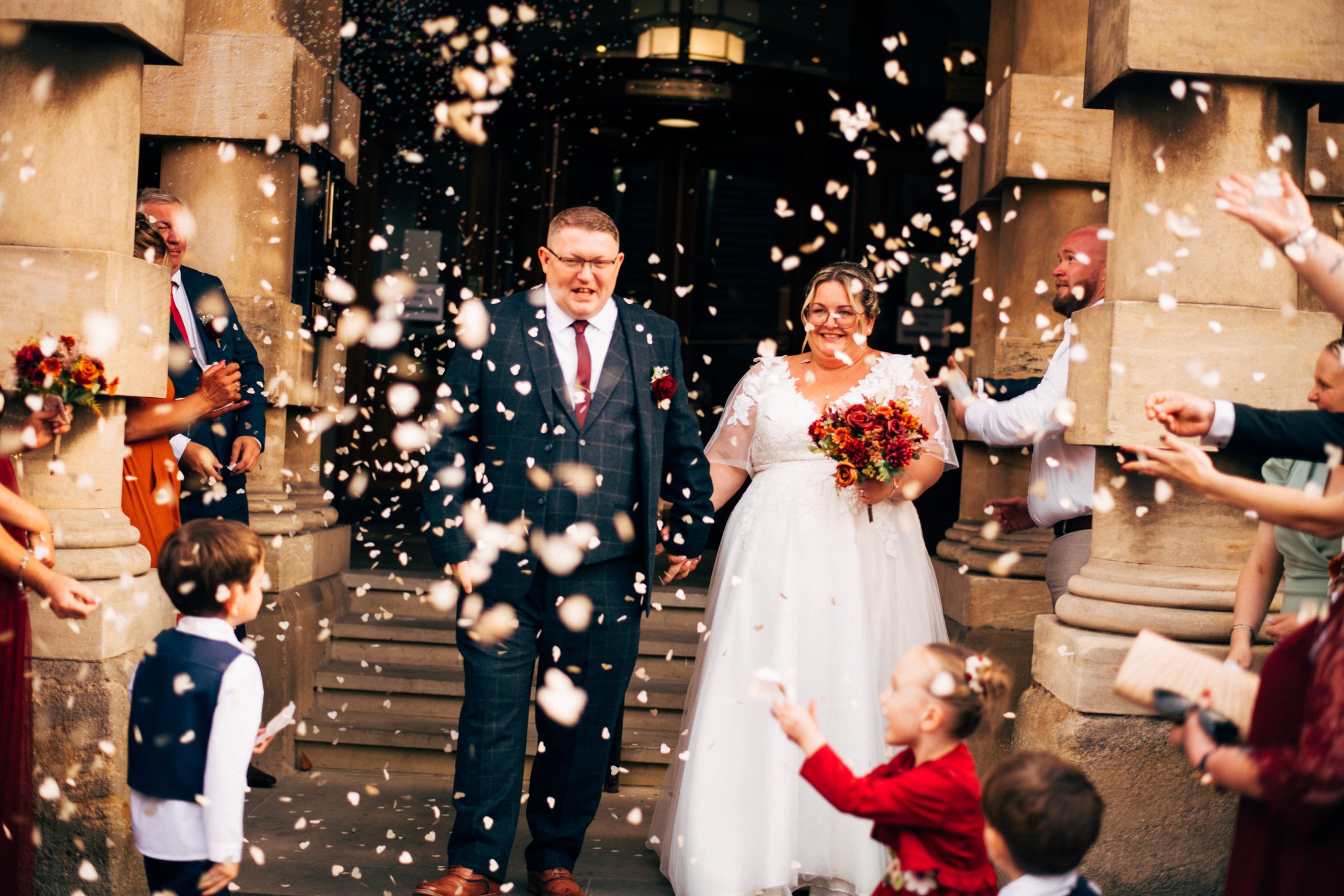 Wedding couple exiting church while guests throw confetti in celebration.