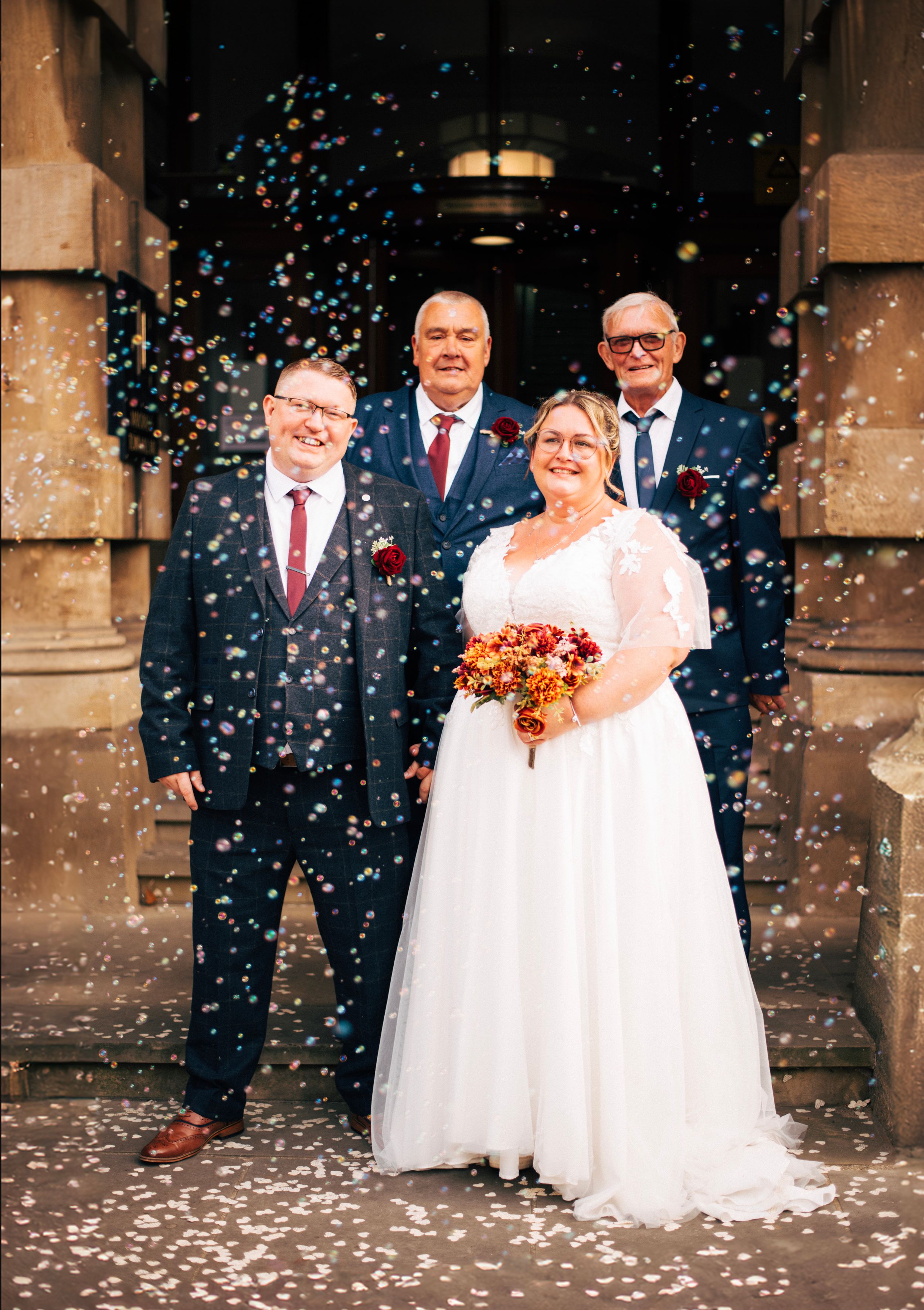 Wedding party standing on church steps surrounded by falling confetti.