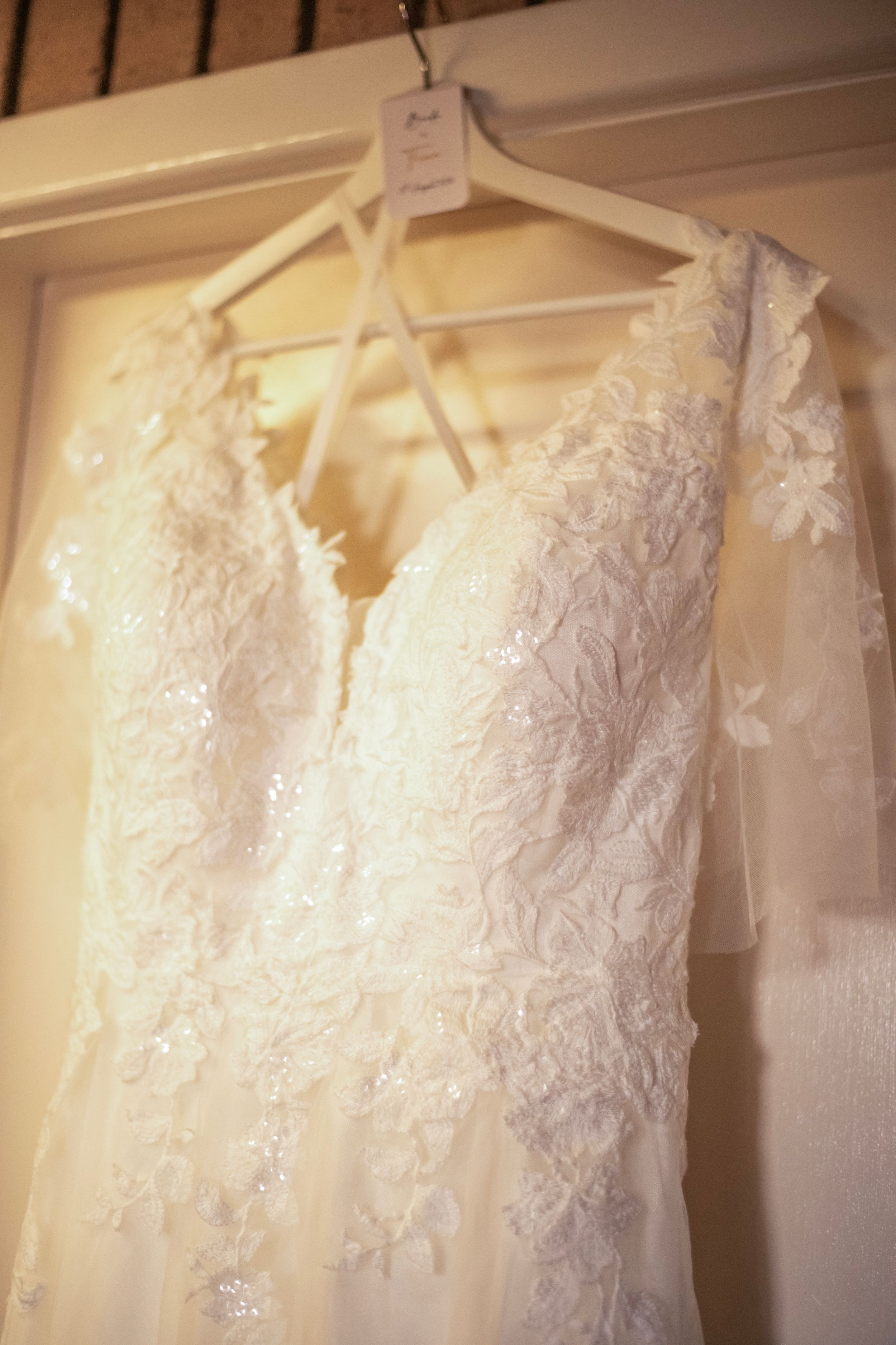 White lace wedding dress with detailed embroidery hanging on display.
