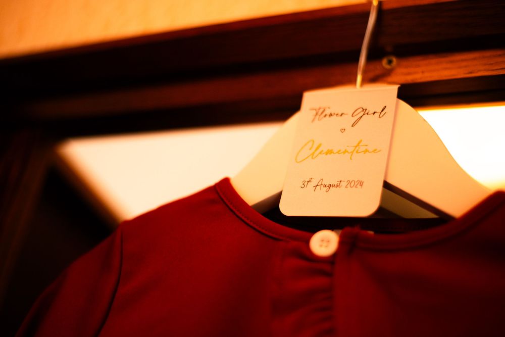 Red bridesmaid dress hanging on a wooden hanger with handwritten label.