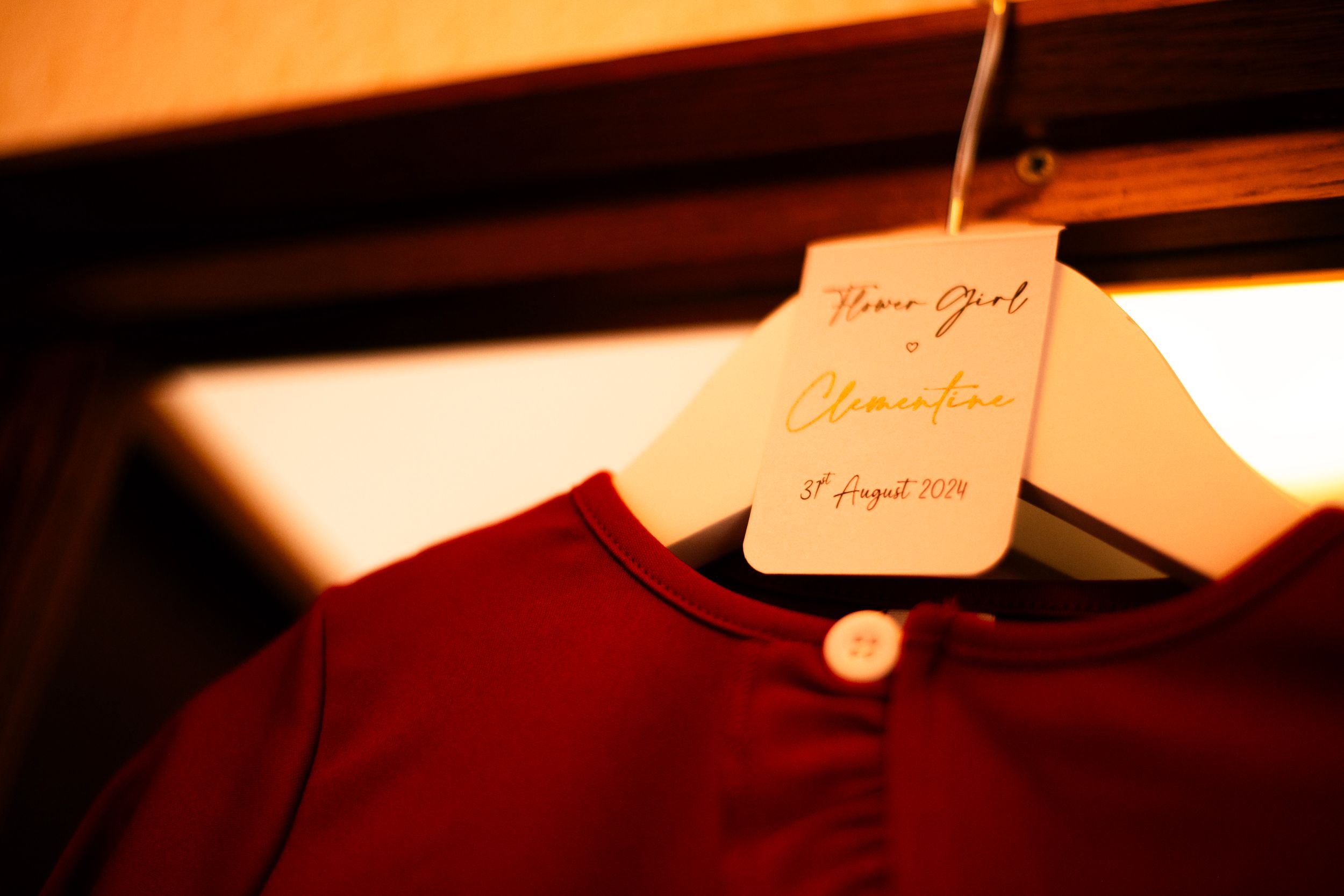 Red bridesmaid dress hanging on a wooden hanger with handwritten label.