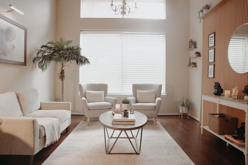 Modern minimalist living room features white walls, hardwood floors, and natural light from large windows creating an airy atmosphere.