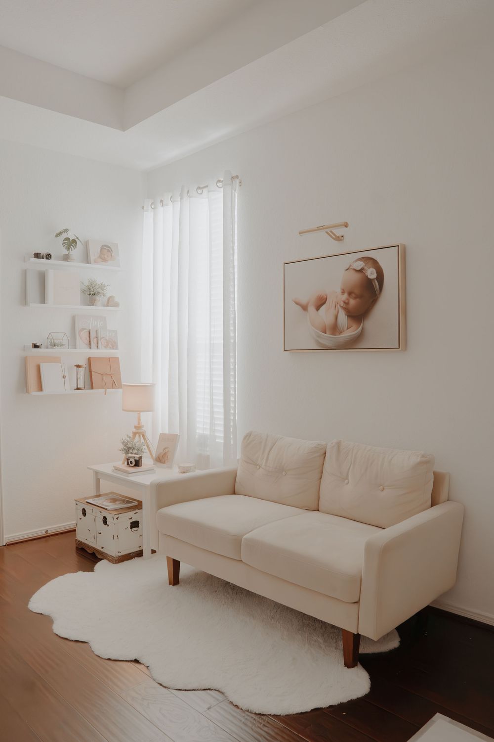 Minimalist white living room with soft furniture, sheer curtains, wooden floors, and neutral wall art.