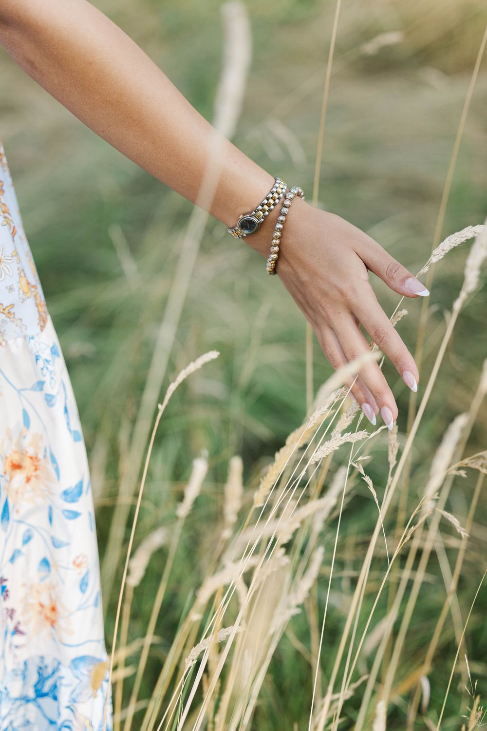 Close-up of teenage girl's hand with bracelets gently touching tall golden wheat grass in a field.