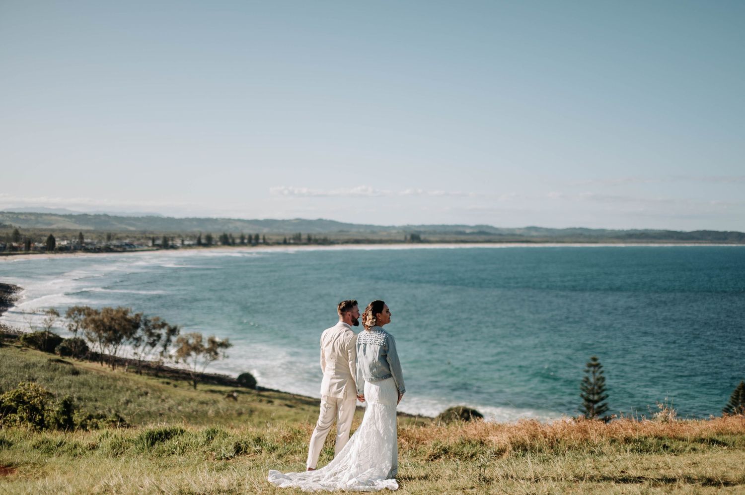 Two people in white dresses overlooking coastal beach view.