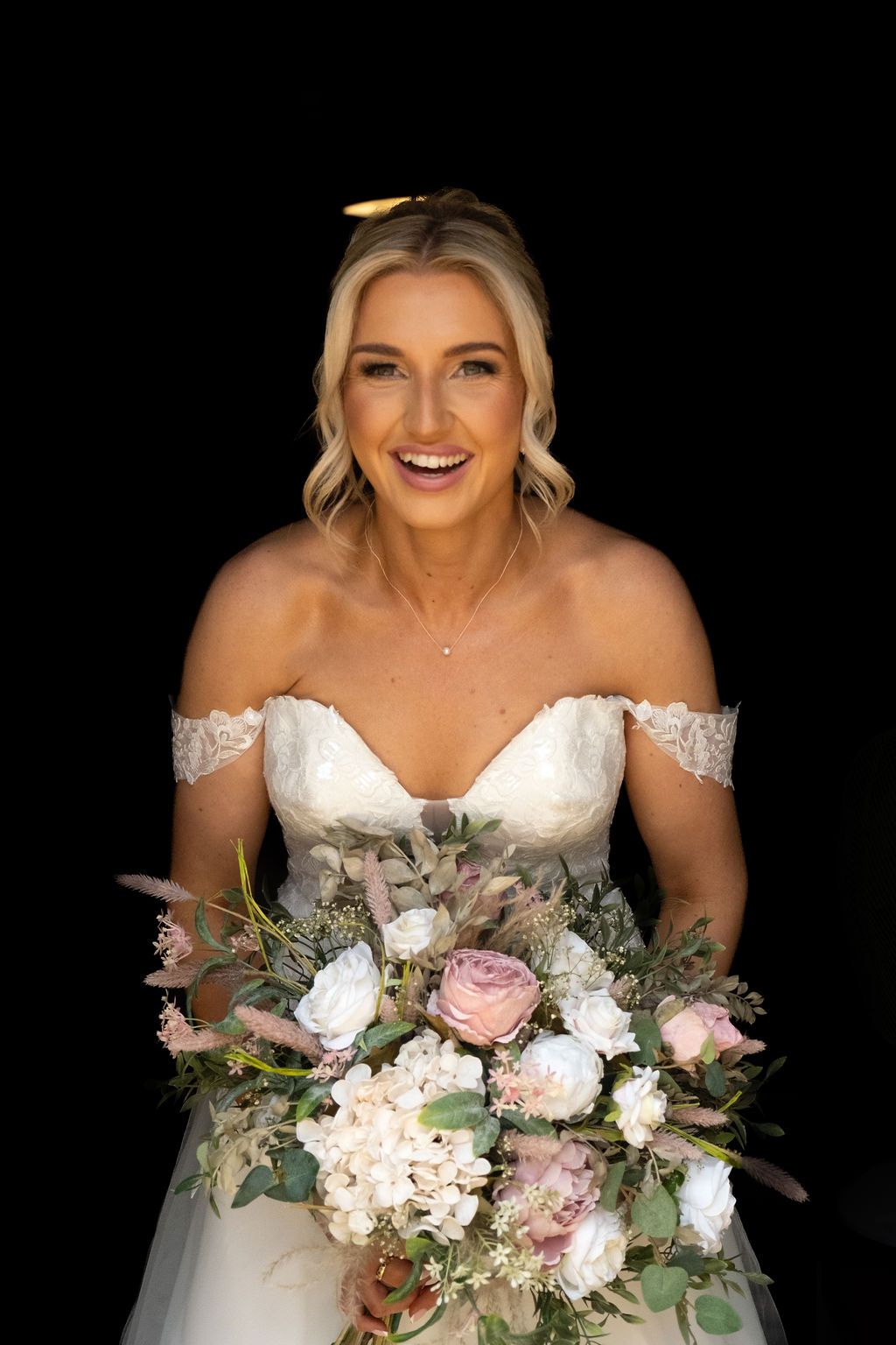 Smiling bride holding a large bouquet of pastel flowers, posing in her wedding dress