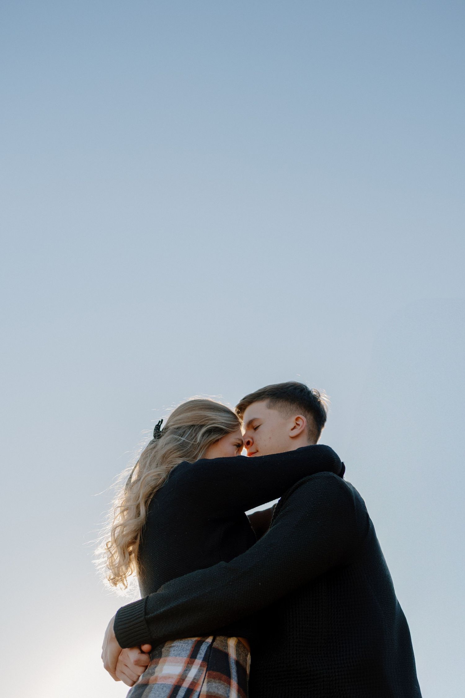 Intimate portrait of couple embracing against blue sky at sunset.