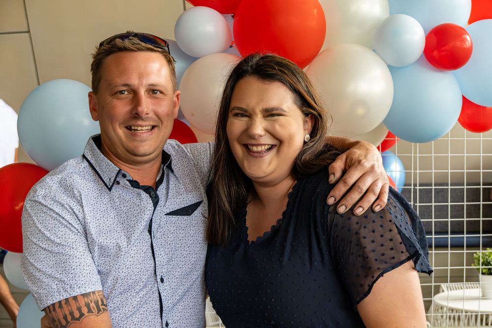 Couple posing together against red, white and blue balloon backdrop.