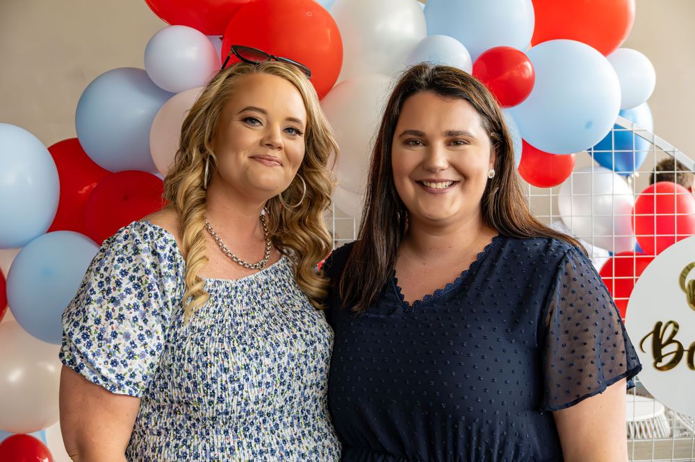 Two people smiling together in front of red, white and blue balloon decoration.