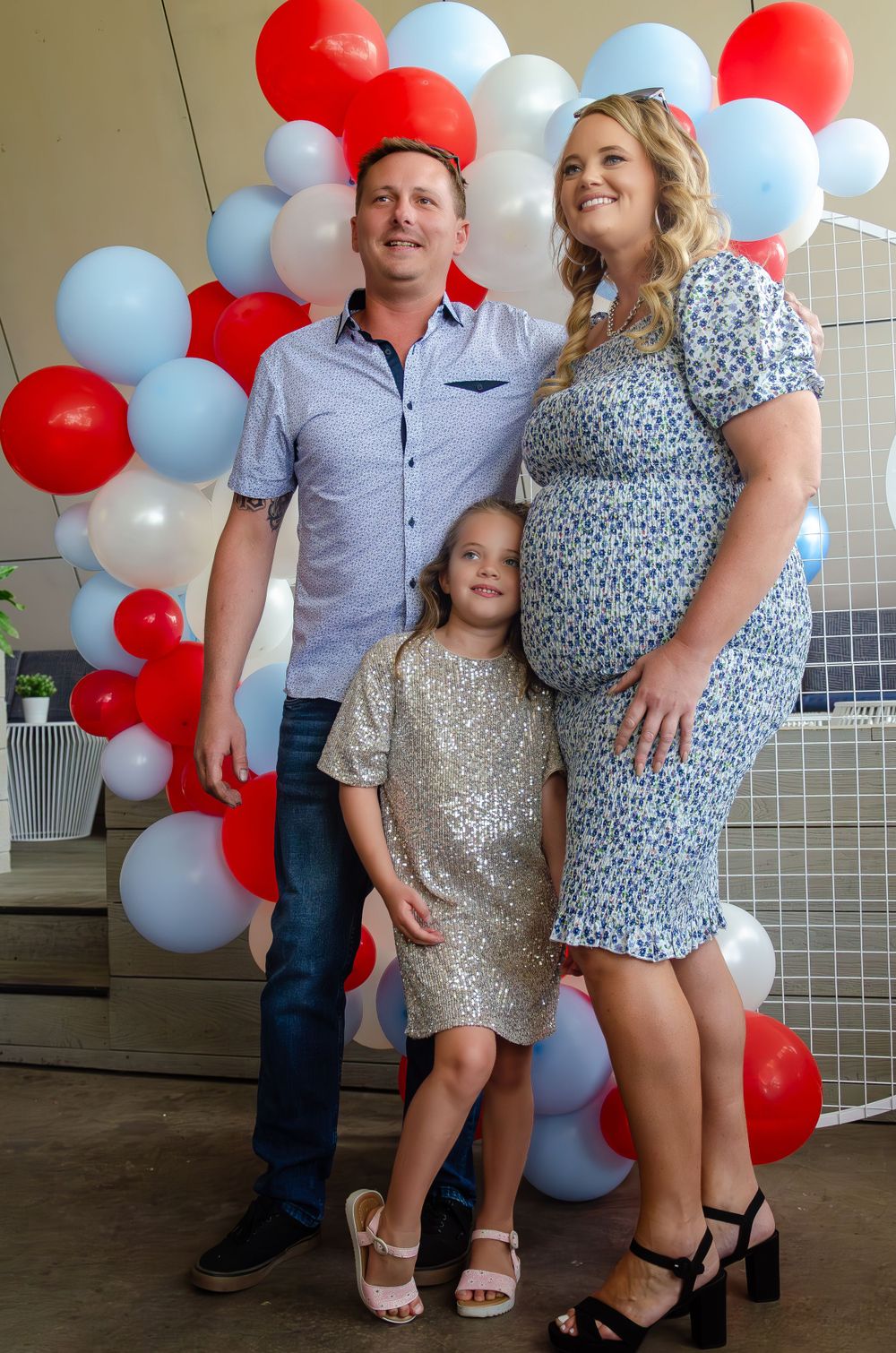 Family posing together against colorful balloon wall at celebration event.