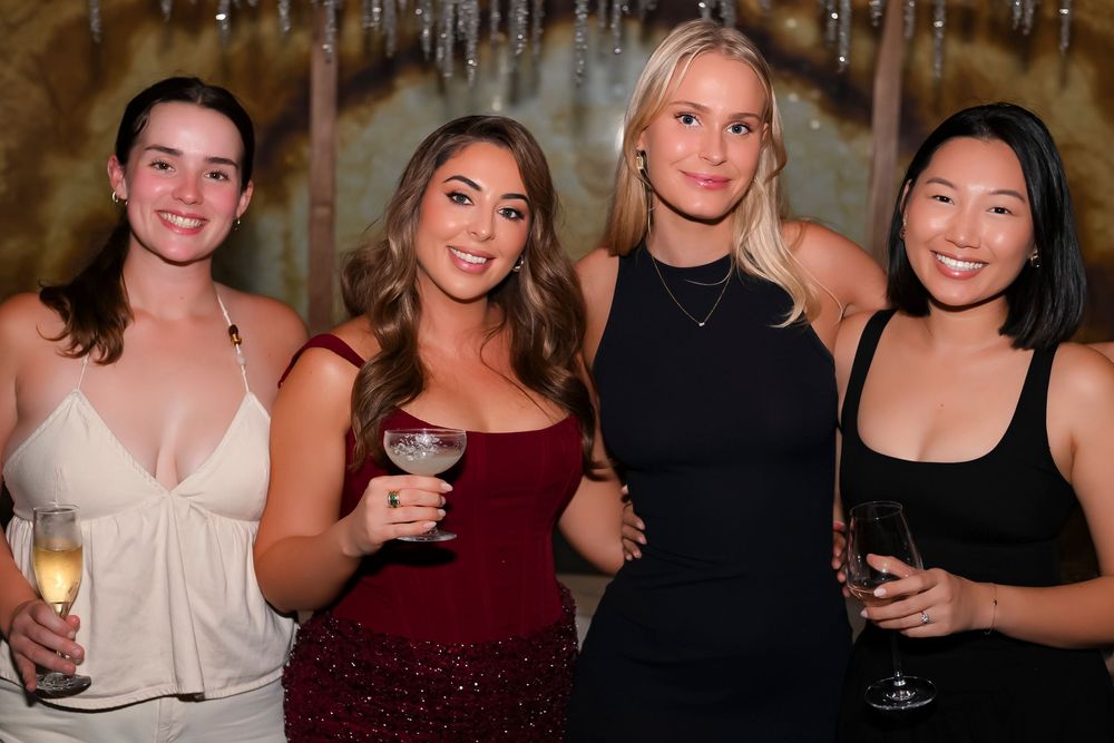 Four women smiling and holding champagne glasses at an elegant evening event.
