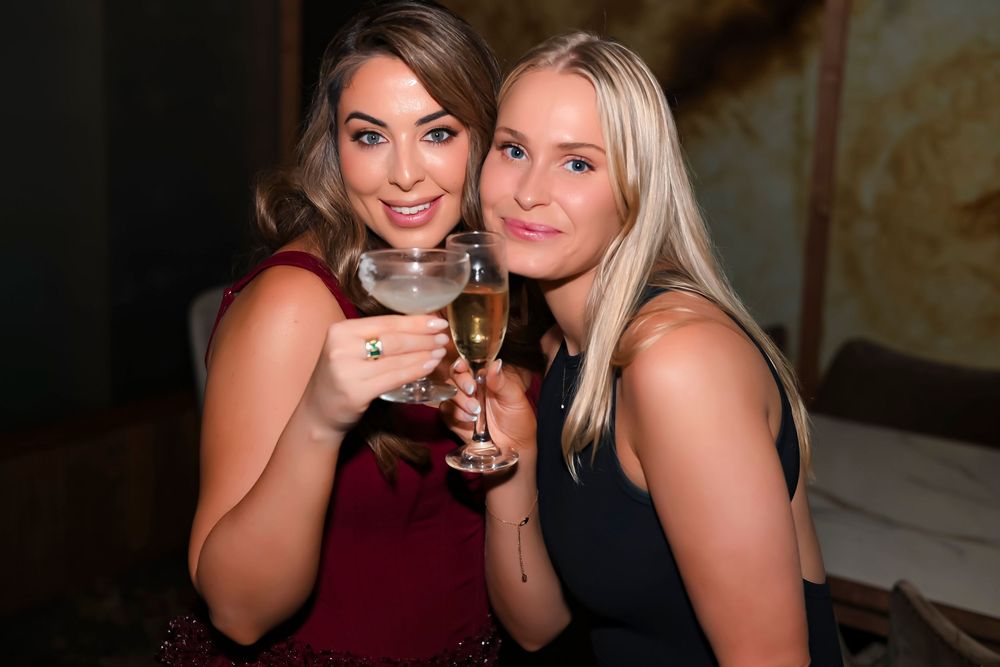 Two women smiling and toasting with wine glasses at a formal evening event.