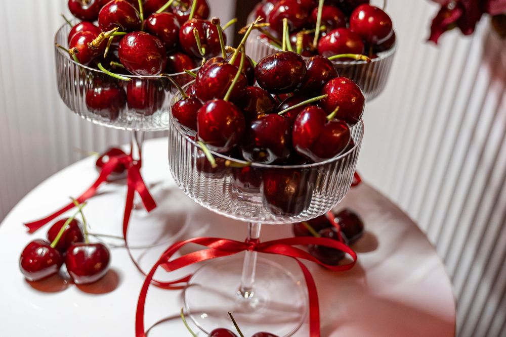 Crystal glasses filled with fresh red cherries tied with red ribbons on a white table.
