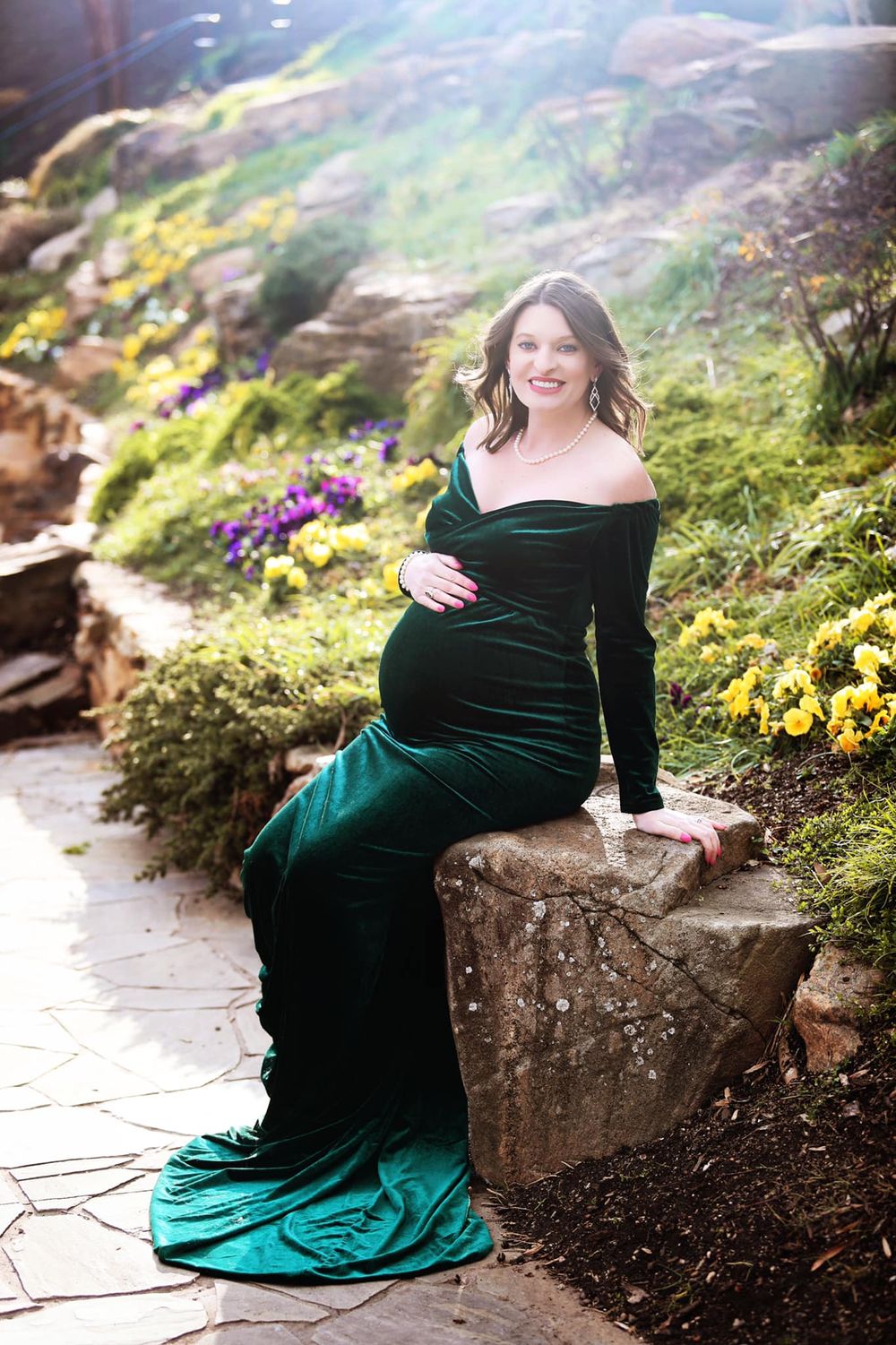 Maternity portrait in emerald velvet gown against garden backdrop.