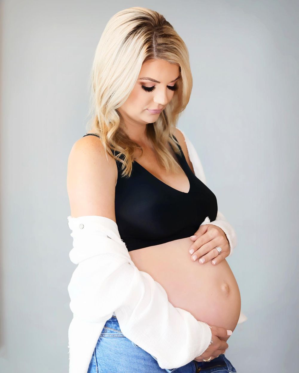Stylish maternity portrait featuring woman in black crop top and white cardigan.