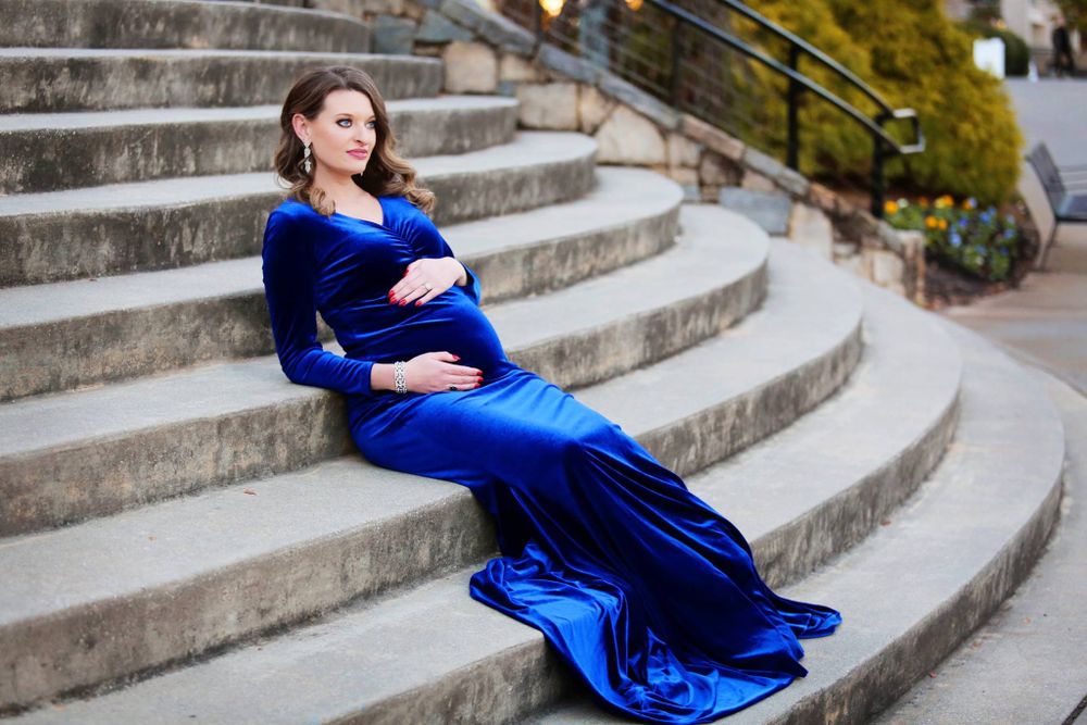 A glamorous maternity photo featuring a flowing blue velvet gown on stone steps.