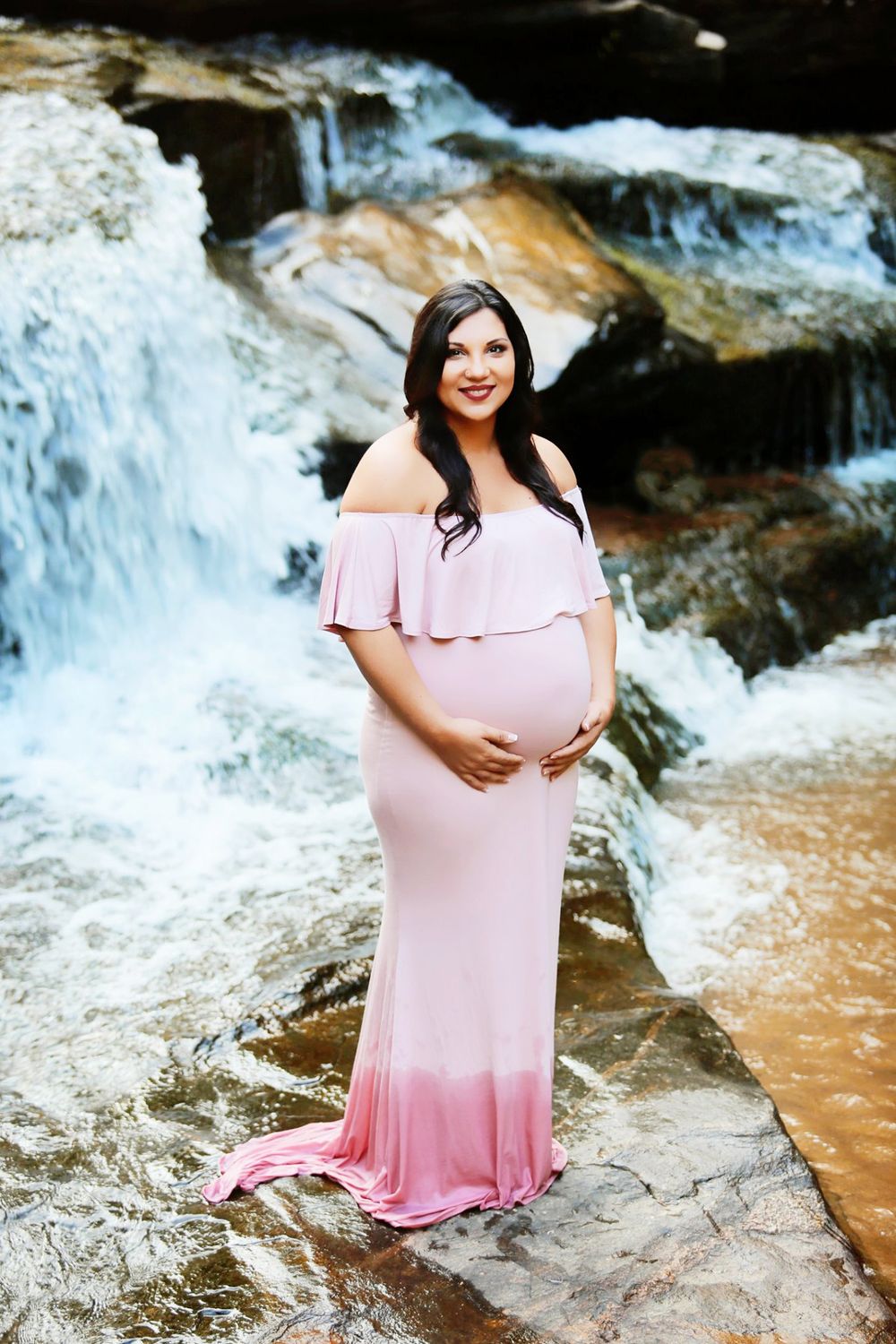 Maternity photo in pink ombre dress against waterfall backdrop.