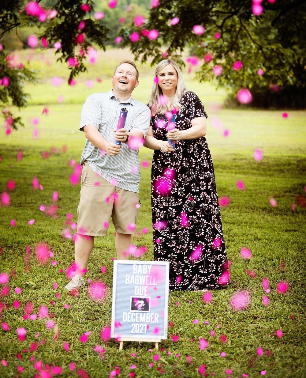 Gender reveal photo with pink confetti floating around couple holding announcement sign.