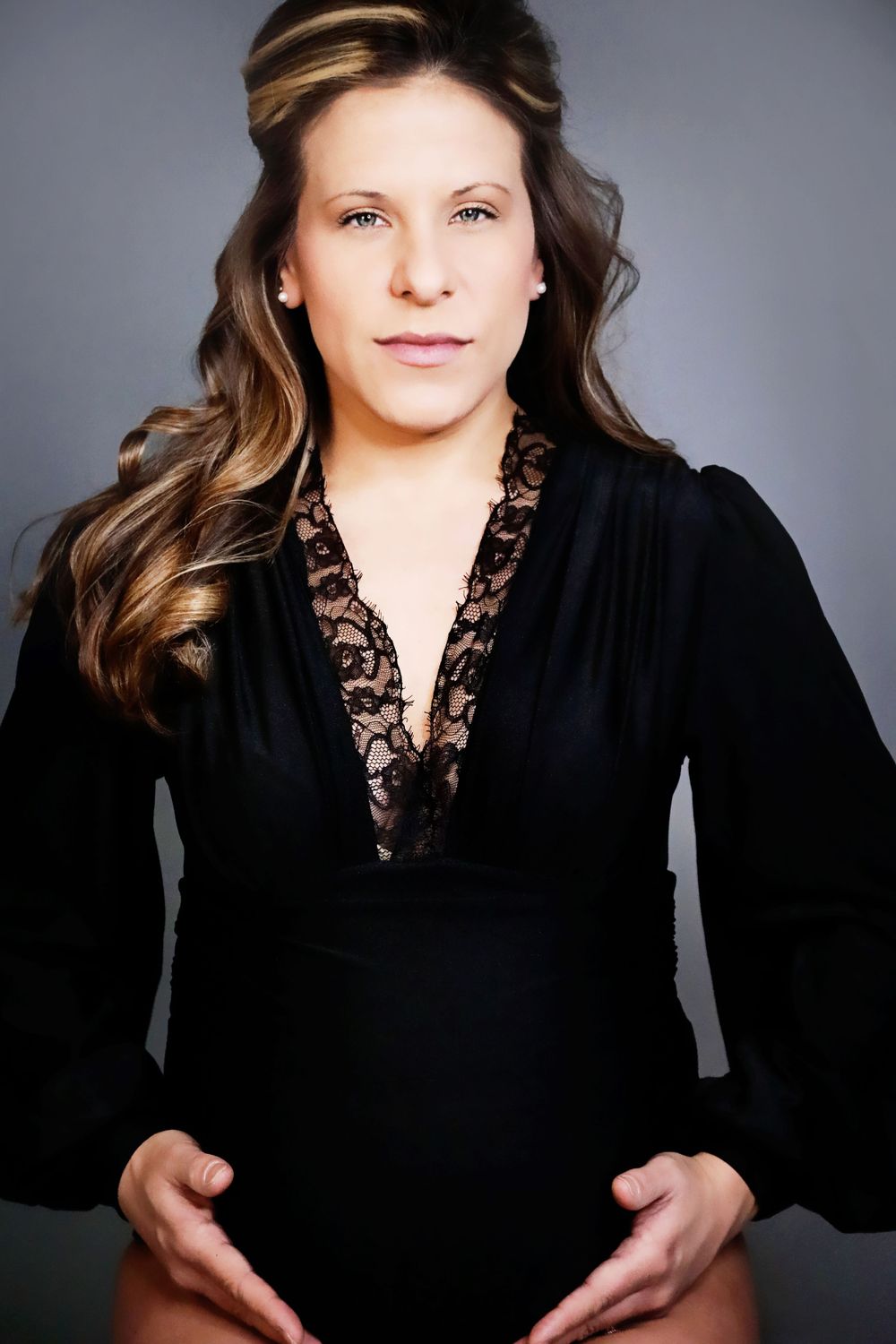 Portrait in black lace-trimmed top with long wavy hair against grey background.