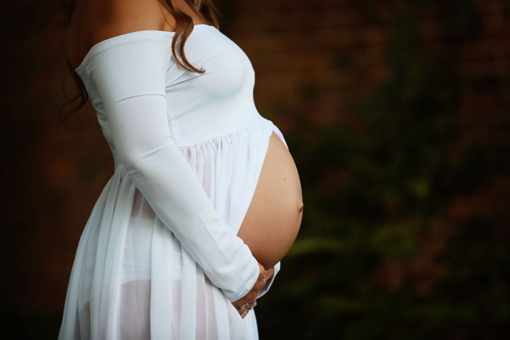 Side view maternity photo showing pregnant belly in white flowy dress.