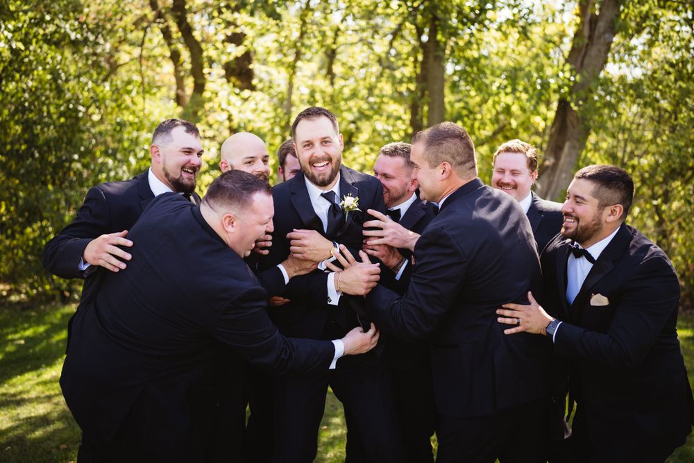 Groomsmen in black suits share a playful moment during outdoor wedding photoshoot.