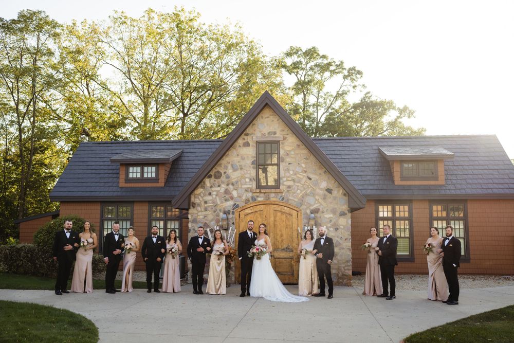 Wedding party lines up for formal photo in front of rustic stone building at sunset.