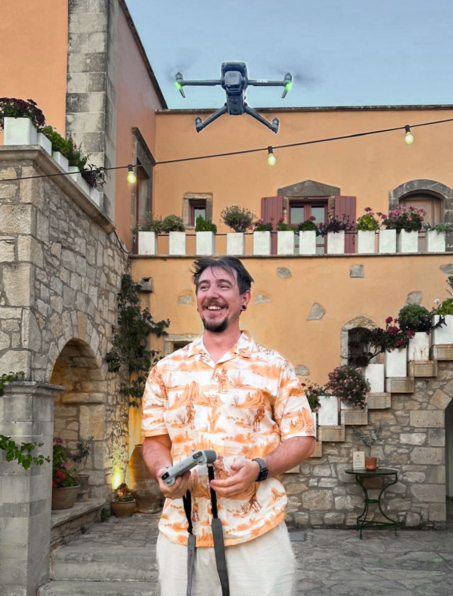 Person in orange floral shirt stands in front of stone archways and peach-colored walls.
