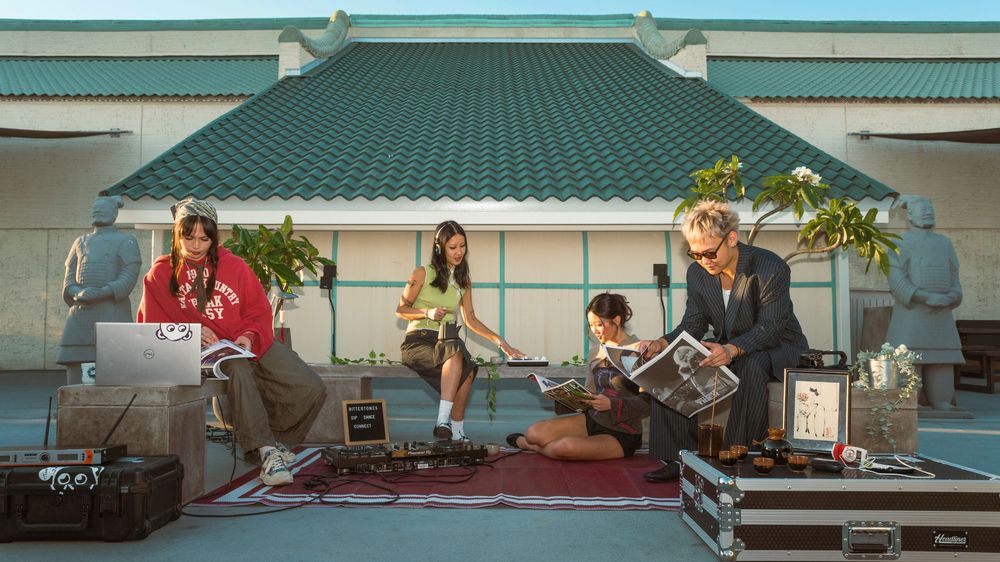 Three musicians perform outdoors on a covered patio with musical instruments and equipment on a red carpet.