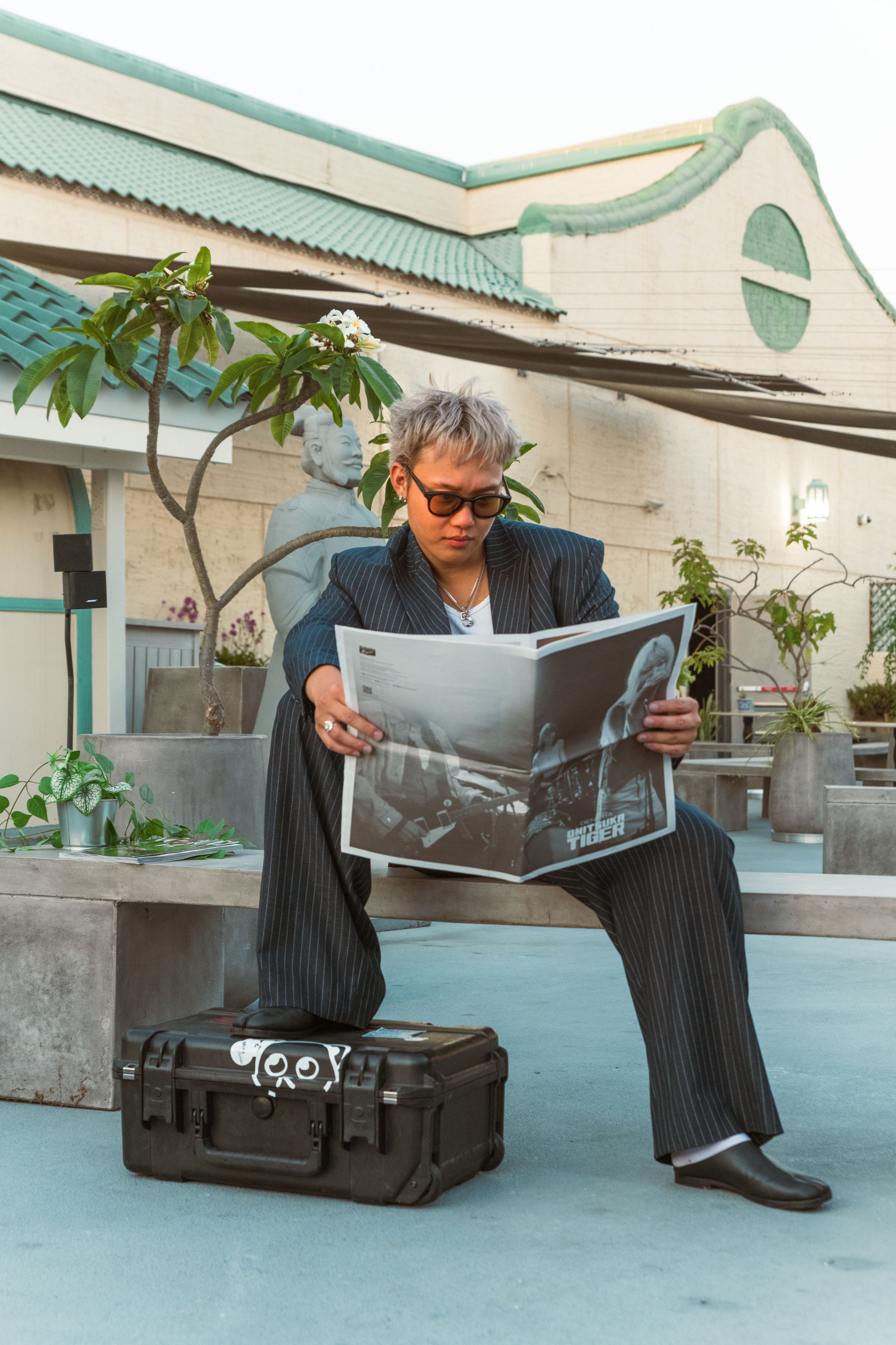 A man sits on an outdoor bench with one leg propped on a container while reading on a rooftop. Photo taken for Bittertones