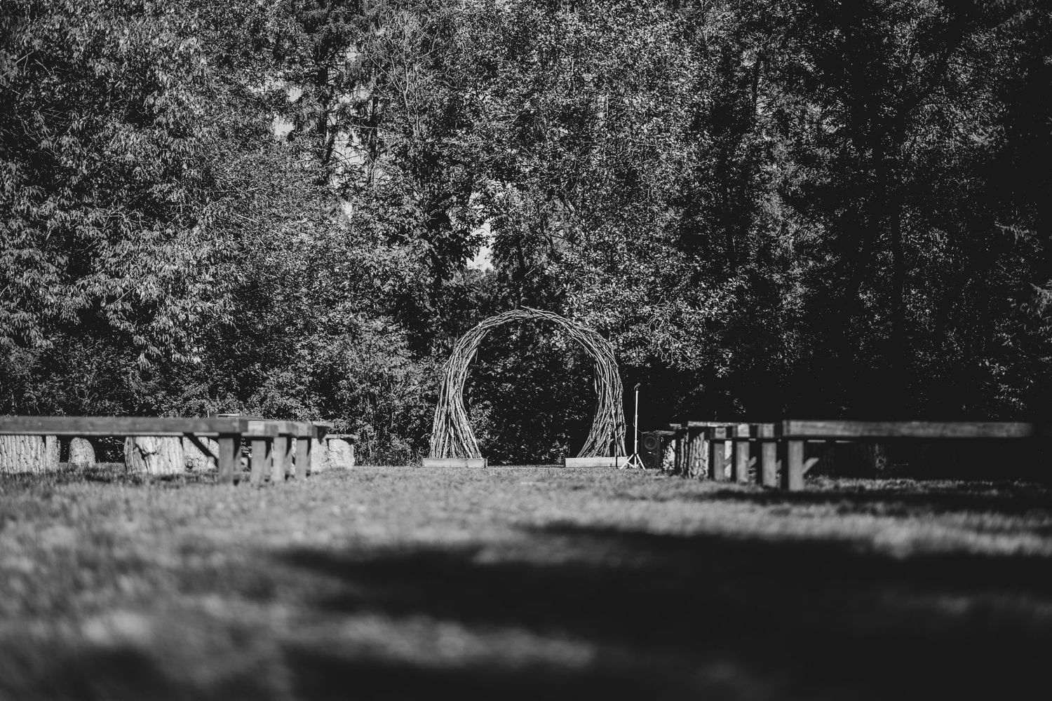 A circular wooden arch stands in a scenic garden setting surrounded by trees in black and white photography.