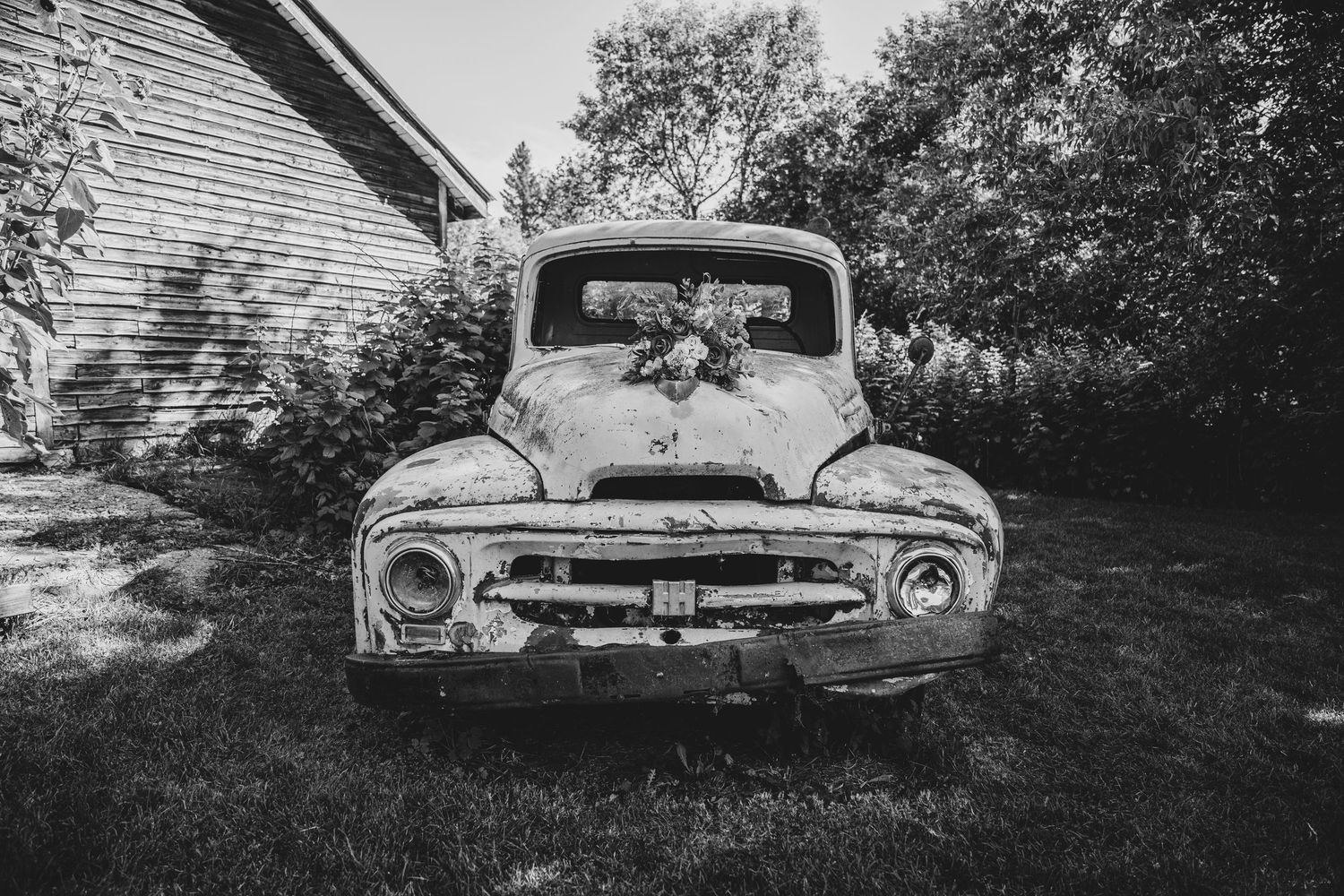 A vintage Ford pickup truck with rustic charm sits parked beside a farmhouse in monochrome.