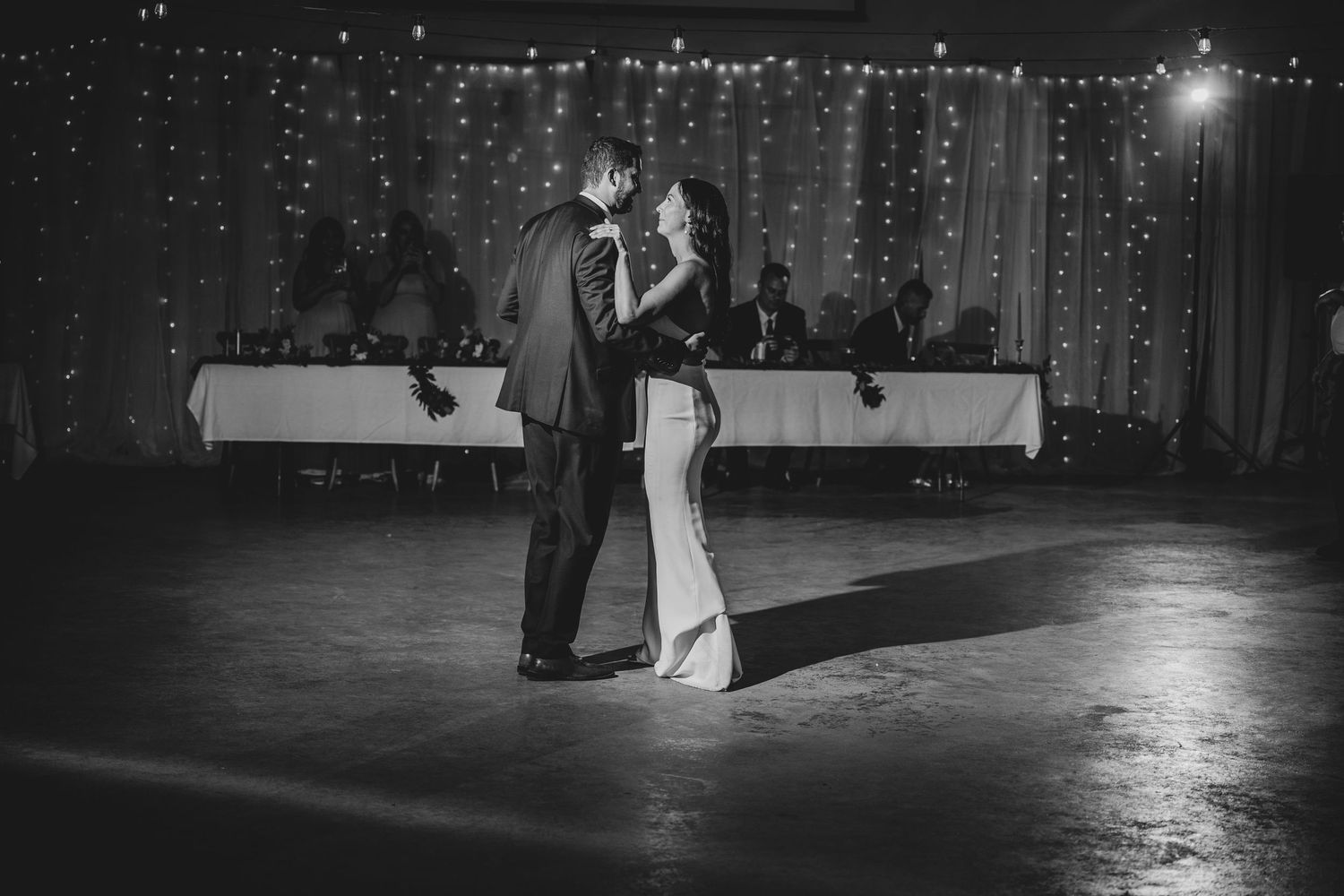 A couple shares their first dance at a wedding reception in elegant black and white photography.