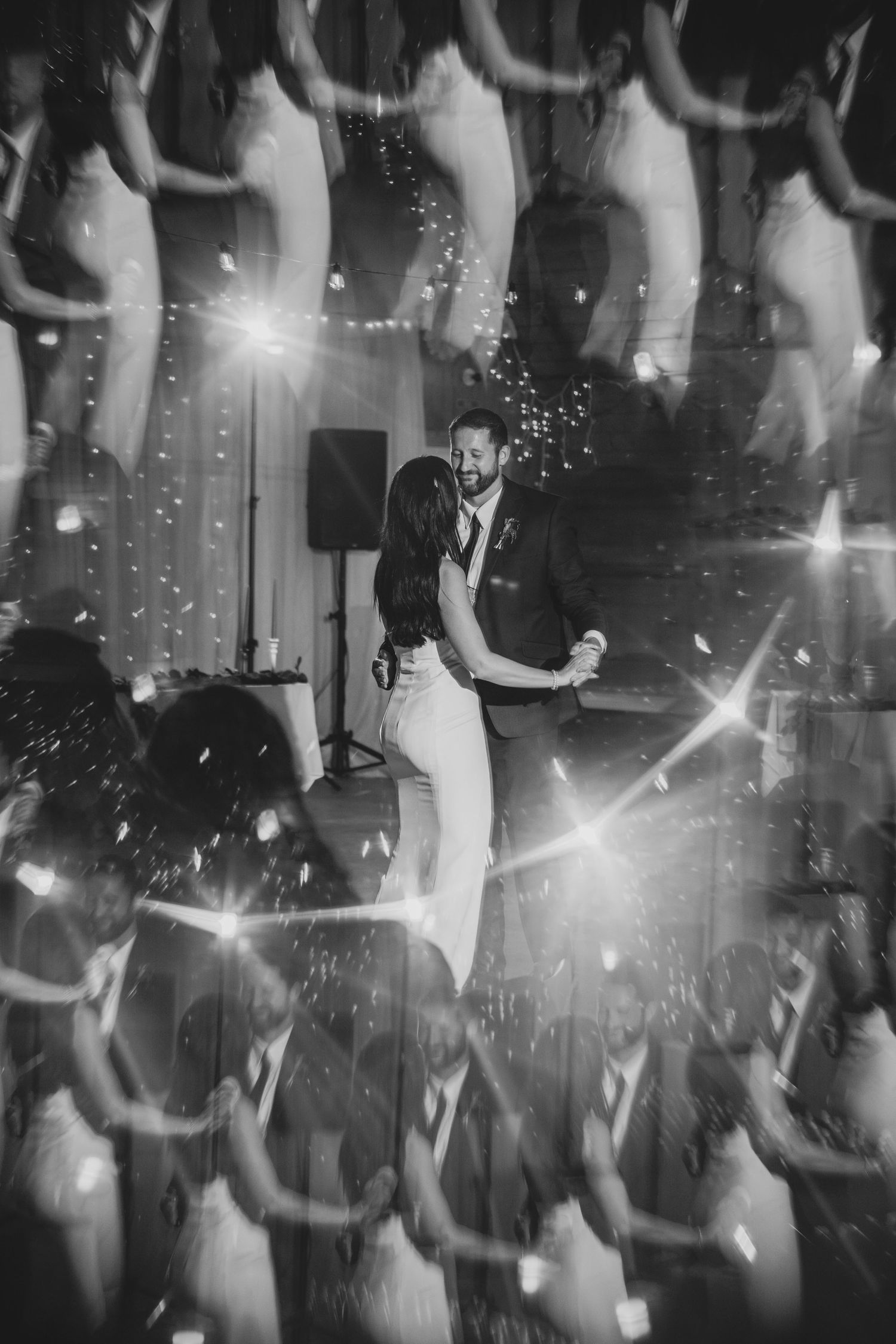 A black and white photo of a wedding reception dance floor with sparkling lights and blurred motion.