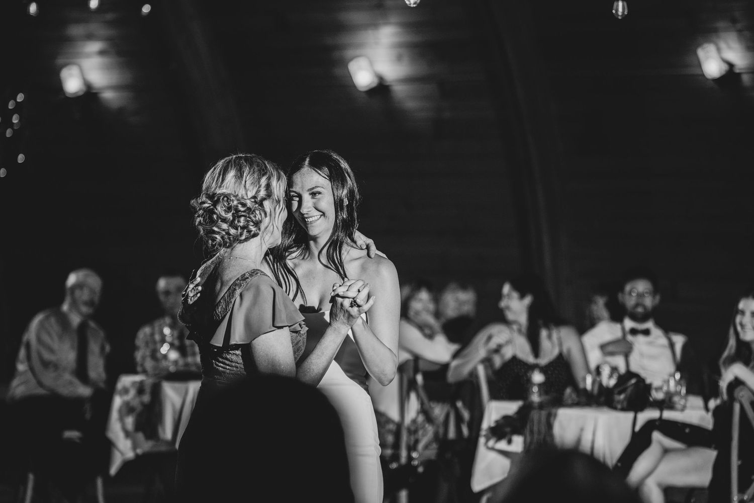A romantic dance taking place in a dimly lit reception venue with guests watching in the background.