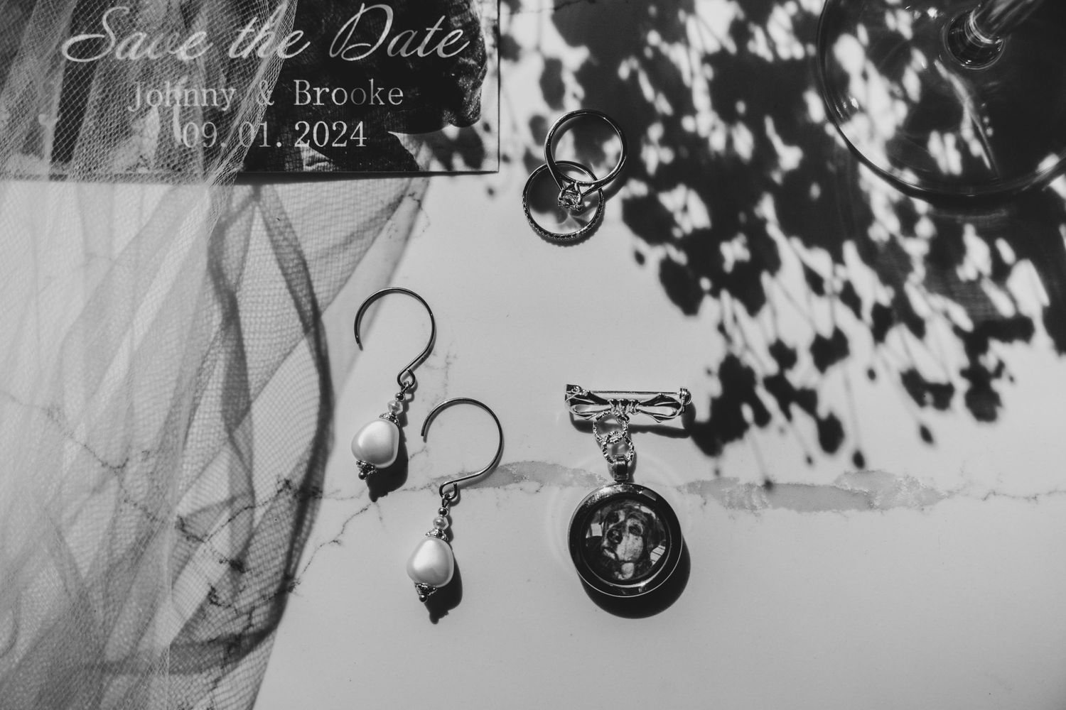 Black and white wedding detail photo showing dangling earrings and military medal against a soft background.