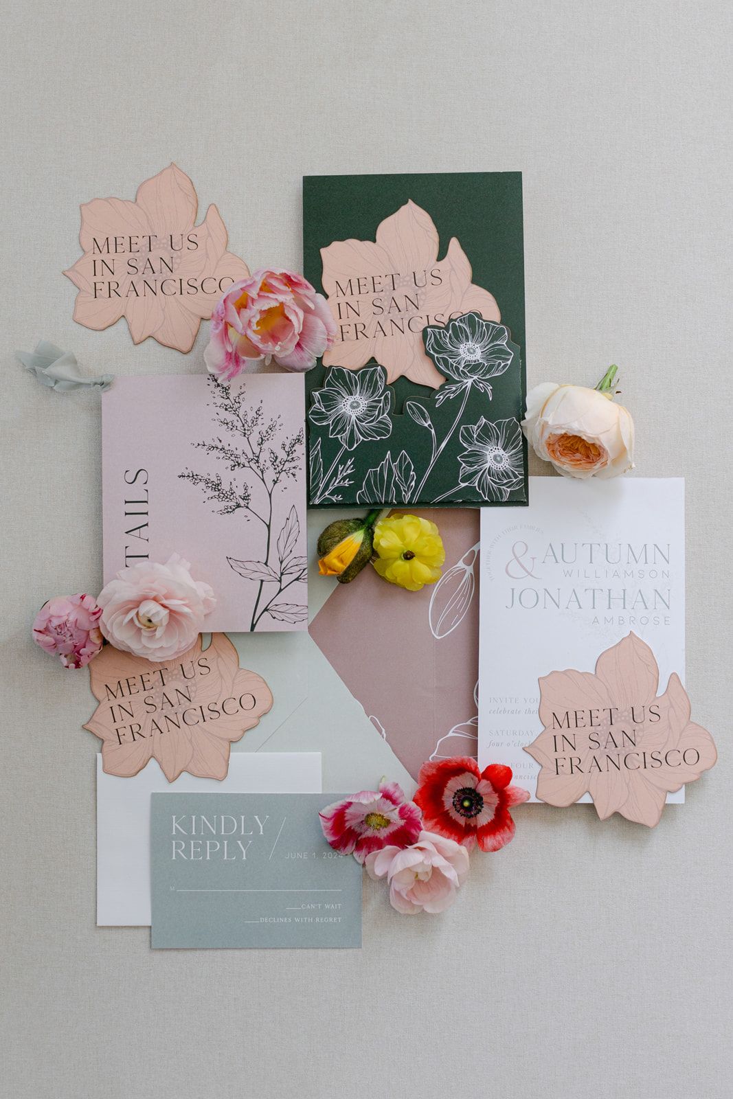 Wedding invitation suite in soft pink and sage green with floral accents and elegant typography arranged on white surface.