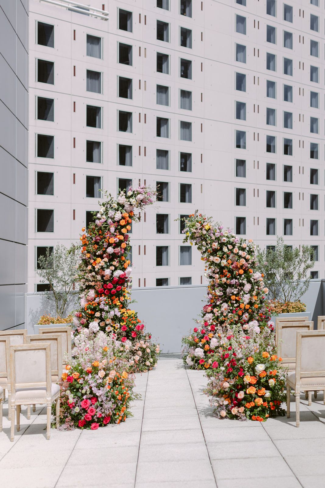 Colorful floral arrangements with pink, orange, and white flowers line up against a modern white building facade.