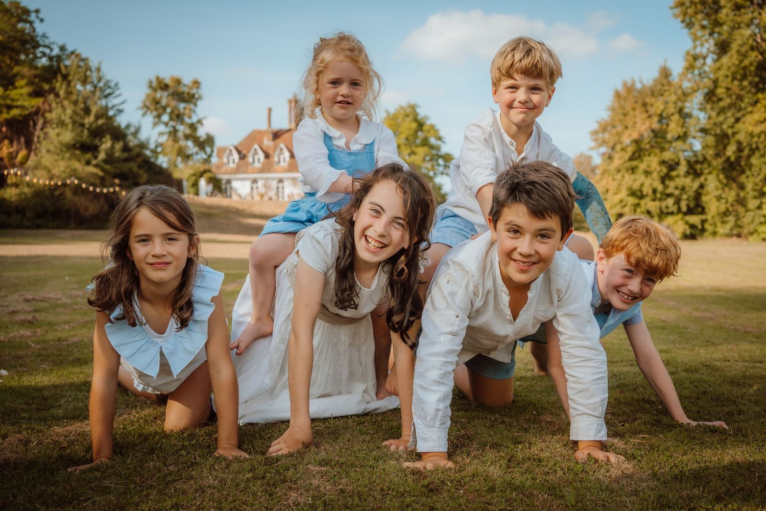 Group playfully poses in a pyramid formation on green grass with autumn trees and a brick building in the background.