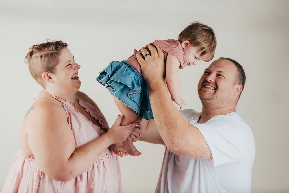 Parents playfully lift their young child in the air while all sharing joyful laughter together.