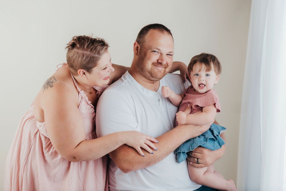 Family sharing a happy candid moment together against a neutral wall.