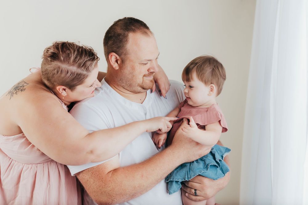 A tender family moment is shared between three people wearing soft pastel colors against a light background.