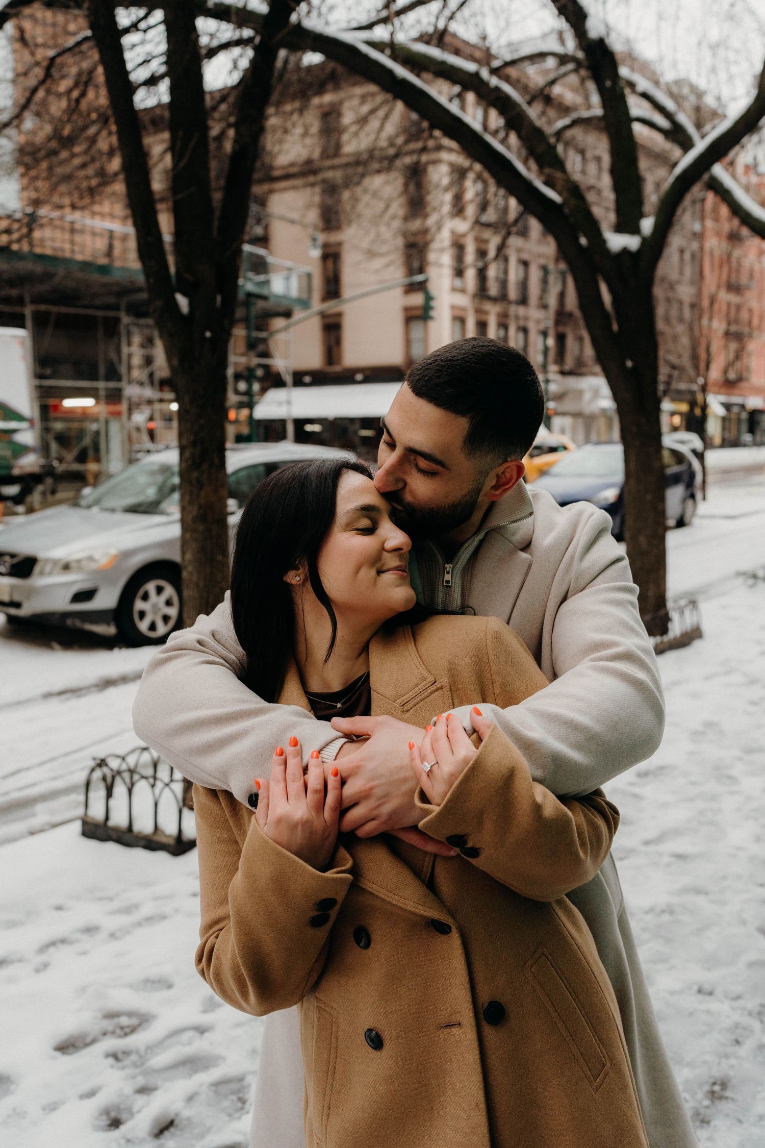Couple sharing intimate winter moment on snowy city street wearing warm coats.