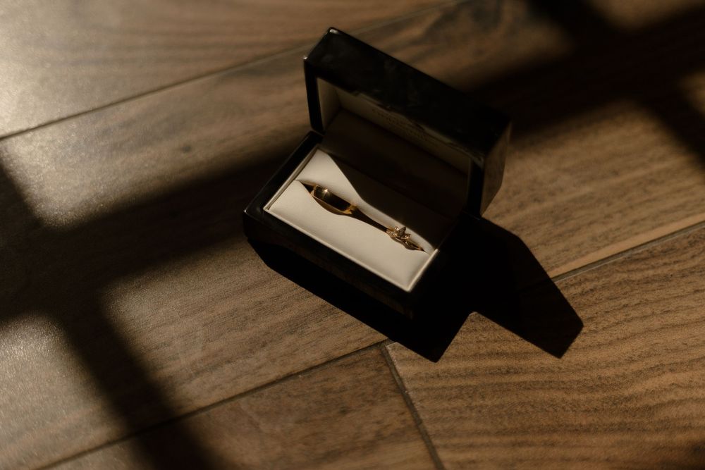 A black gift box with a gleaming silver pen inside rests on a dark wooden surface casting dramatic shadows.